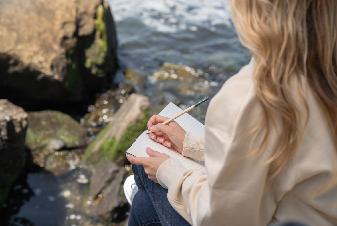 Open notebook on a wooden bench beside calm water, representing self-reflection and inner healing.