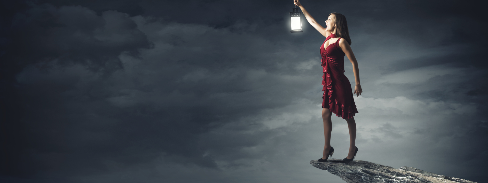 Woman in red dress stands on a rocky cliff, holding a lantern out into a stormy night sky