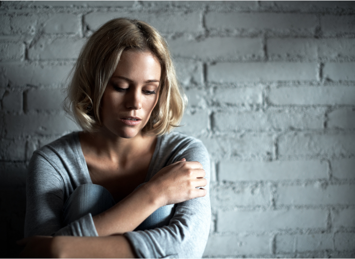 Woman sits in deep thought, arms wrapped around her knees